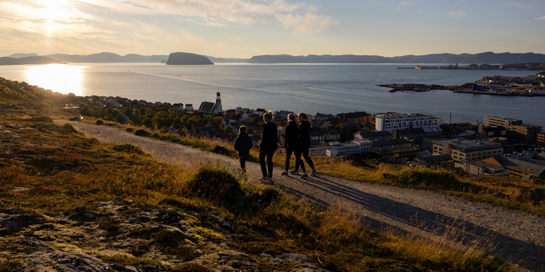 Fire personer ute i en åsside ved solnedgang. Hammerfest ligger nedenfor.