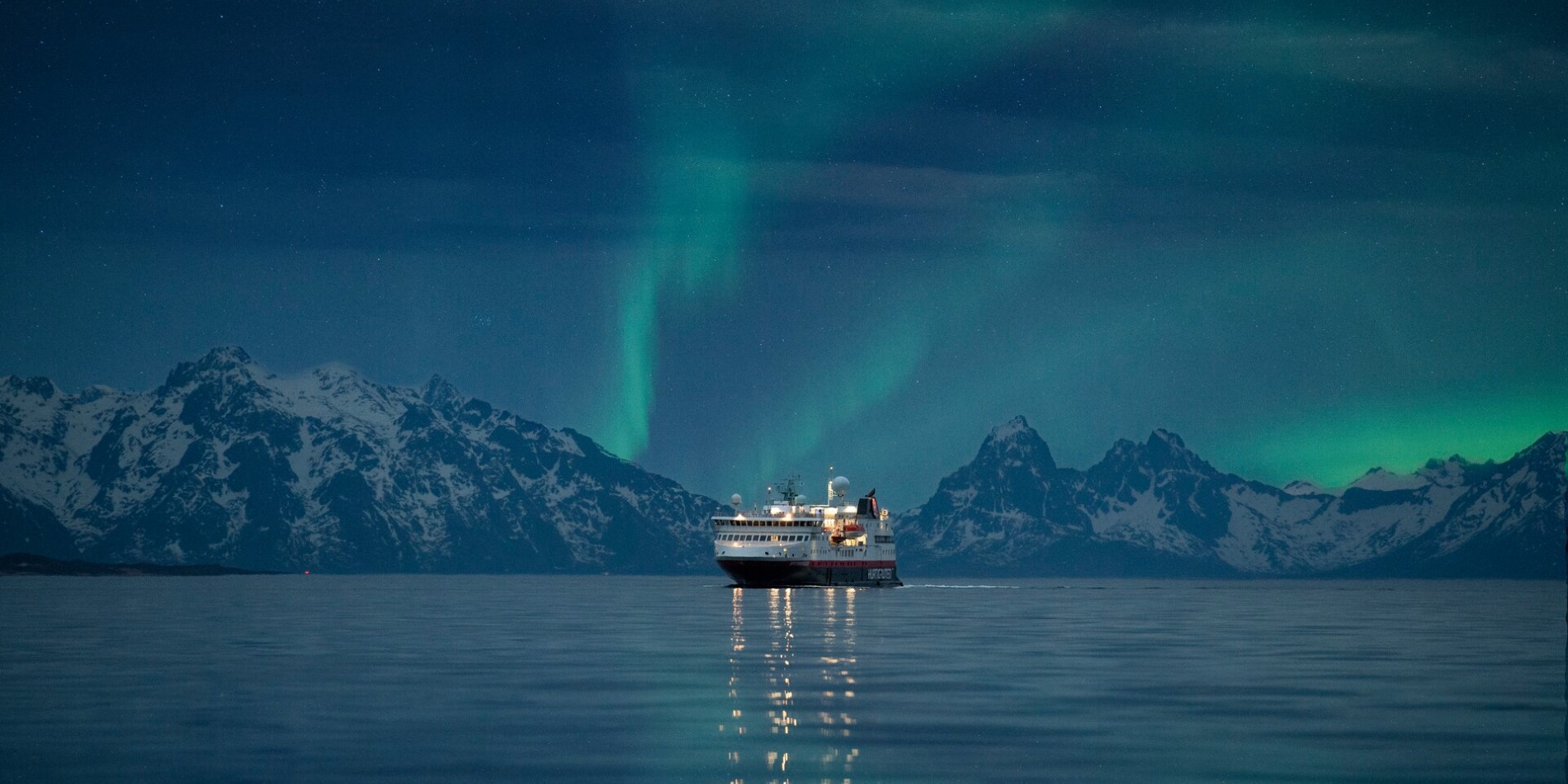 Et Hurtigrutenskip som seiler i Norge med nordlyset på himmelen ovenfor